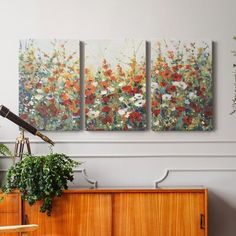 three paintings are hanging on the wall above a dresser in a room with a plant