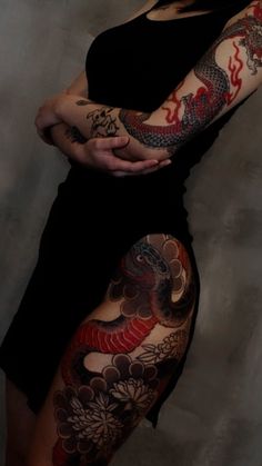 a woman with dragon tattoos on her arm and leg, standing in front of a wall