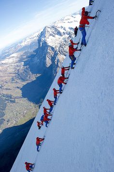 several skiers are climbing up the side of a snowy mountain with mountains in the background