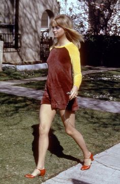 a woman walking down the sidewalk in her red and yellow dress with orange sleeves on