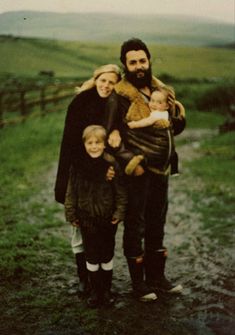 a man and two children standing on a dirt road in front of a green field