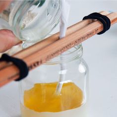 someone is pouring sugar into a glass jar with orange juice in it and two wooden sticks sticking out of the top