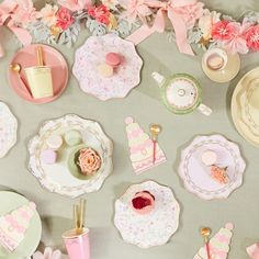 a table topped with lots of pink and white plates covered in paper flowers next to cups and saucers