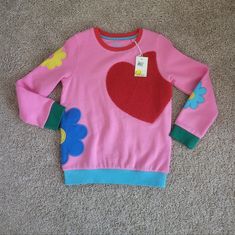 Heavy Pink Sweatshirt Has Multi-Colored Bands, Red Neck, Green Cuffs, And A Blue Banded Waist. The Front Has An Oversized Heavy Red Heart Applique, With Heavy Mod Flower Appliques On Both Sleeves And The Left Side That Wraps Around To The Back. Made Of A Soft Cotton Blend. Size 7/8 Would Look Awesome Paired With Her Favorite Jeans Or Skirt Nwt Never Worn Excellant Condition No Damage Boden Fun Red Tops For Fall, Playful Cotton Winter Tops, Playful Crew Neck Sweatshirt For Playwear, Playful Winter Cotton Tops, Playful Cotton Tops For Winter, Playful Pink Crew Neck Sweater, Winter Crew Neck Sweatshirt For Playwear, Winter Playwear Crew Neck Sweatshirt, Winter Playwear Sweatshirt Crew Neck