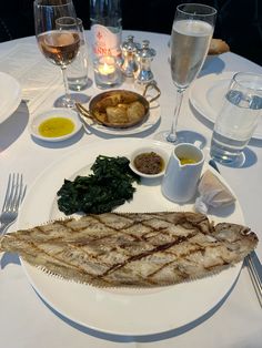 a white plate topped with fish next to wine glasses and other foods on a table