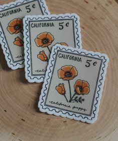 three stamps with orange flowers on them are sitting on a tree stump in front of the camera