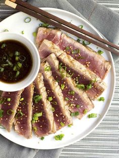 a plate topped with sliced meat next to chopsticks and a bowl of soup