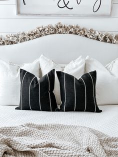 a white bed topped with black and white pillows next to a framed sign that says love