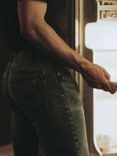 a man is standing in front of an open refrigerator with his hand on the door