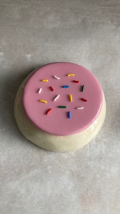 a pink frosted cake with sprinkles sitting on top of a table