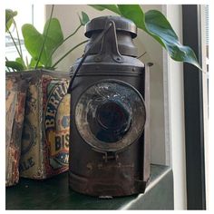 an old camera sitting on top of a window sill next to a potted plant