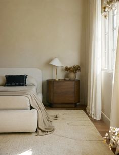 a white bed sitting next to a window on top of a wooden dresser in a bedroom