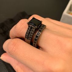 a woman's hand with two rings on top of her finger and the ring has black diamonds in it