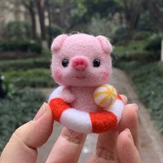 a hand holding a small pink teddy bear with an orange life preserver in it's palm