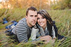 a man and woman laying on the ground in tall grass with their arms around each other