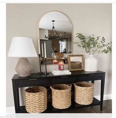 a console table with three baskets on it and a mirror in the corner behind it