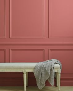 a white bench with a blanket on it in front of a pink wall and wooden floor