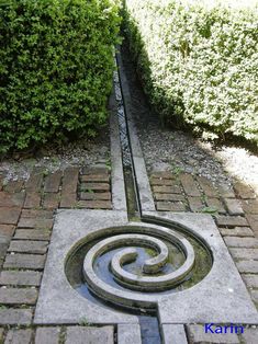 a stone walkway with a spiral design on it and bushes in the backgroud