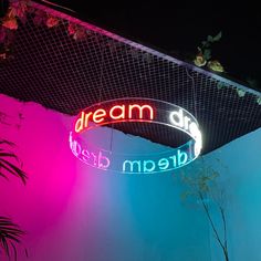 a neon sign hanging from the side of a building next to a potted plant