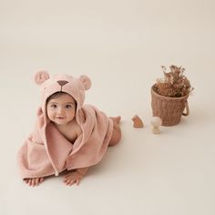 a baby wrapped in a teddy bear towel next to a potted plant and stuffed animal