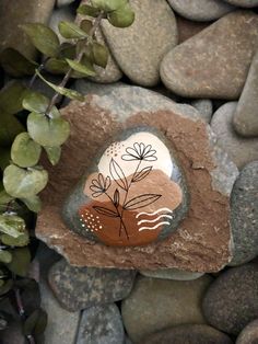 a rock with a plant painted on it sitting next to some rocks and green leaves