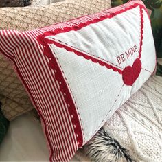 a red and white pillow sitting on top of a bed next to a stuffed animal