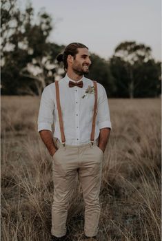 a man standing in the middle of a field wearing suspenders and a bow tie