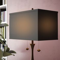 a lamp on a table next to a book shelf and potted plant in the corner