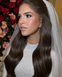 a woman with long brown hair wearing a veil and diamond earrings on her wedding day