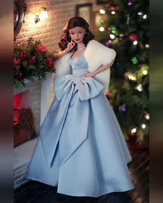 a barbie doll dressed in a blue gown and fur stoler standing next to a christmas tree