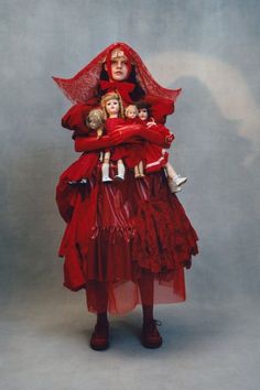 a woman in a red dress holding two dolls and wearing a long veil over her head