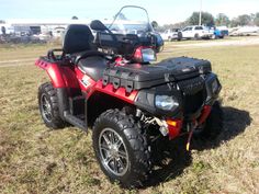 a red four - wheeler parked in a field with other vehicles behind it and on the grass