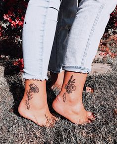 two people with tattoos on their feet standing next to each other in front of flowers