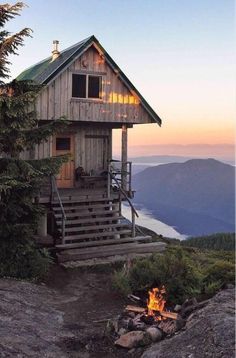 a small cabin on top of a mountain with a fire pit in the foreground