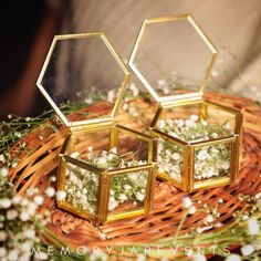 three small gold hexagonal boxes sitting on top of a wicker basket filled with baby's breath flowers