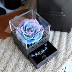 a blue rose in a clear box on a white blanket next to two other boxes