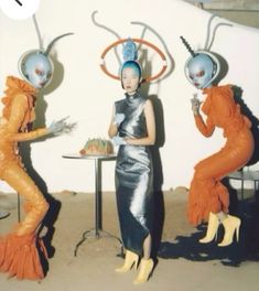 three women dressed in costumes standing next to each other near a table with food on it