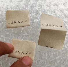 two pieces of cloth with the words lunayx and lunaay printed on them are being held by someone's fingers