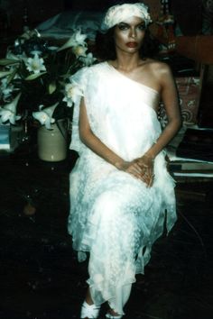 a woman in a white dress sitting next to flowers