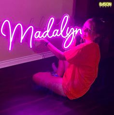 a woman sitting on the floor holding up a neon sign that reads madly in front of her