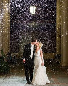 a bride and groom kissing under falling snow at their wedding reception in the grand hall