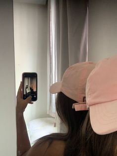 a woman taking a selfie in front of a mirror with her cell phone and hat on