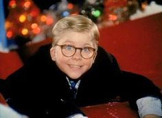 a man wearing glasses and a black coat sitting on a red couch with christmas lights in the background