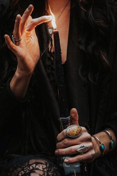 a woman holding a lit candle in her right hand and wearing rings around her wrist