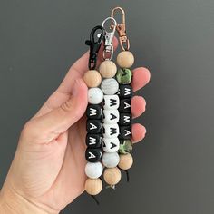 a hand holding a key chain made out of wooden beads and black keys with white letters on them