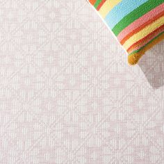 a colorful striped pillow sitting on top of a pink floor next to a white wall