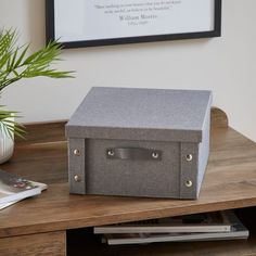 a grey box sitting on top of a wooden table next to a plant and magazine