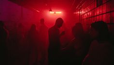 a group of people standing in a dark room with red light coming from the ceiling