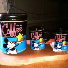 three mickey mouse coffee mugs sitting on top of a wooden table next to each other