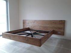 a wooden bed frame sitting in the middle of a room next to a large window